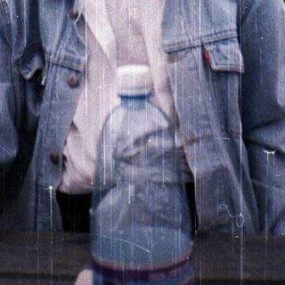 Woman smiling in light rain, holding water bottle.