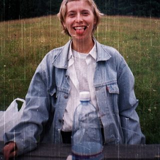 Woman smiling in light rain, holding water bottle.