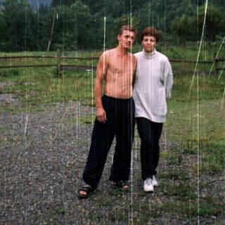 Two men standing under artificial rain in an outdoor setting.