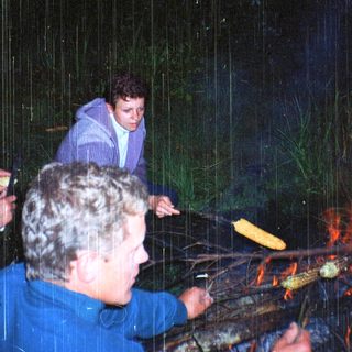 People roasting corn over an open fire in rain.