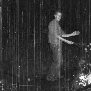 Man standing under artificial rain in dark.