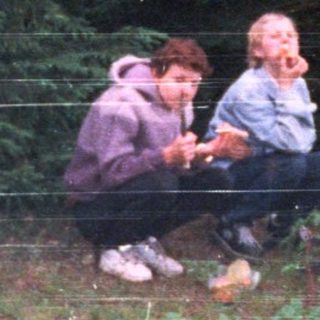 People sitting on bench in forested outdoor area.