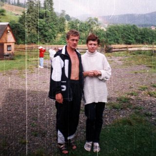 Two people standing outdoors in rainy countryside.