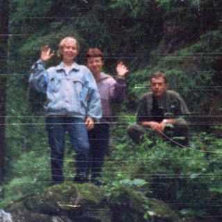 People standing near a waterfall in forested area.