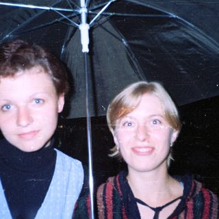 Two women standing together under an umbrella.