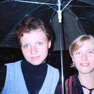 Two women standing together under an umbrella.
