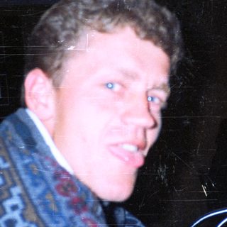 Man in patterned sweater holding drink at night event.