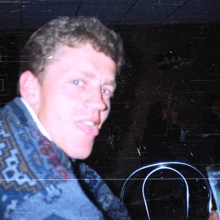 Man in patterned sweater holding drink at night event.