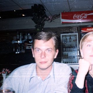 Two people posing indoors near Coca-Cola sign.