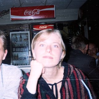 Two people posing indoors near Coca-Cola sign.