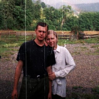 Two people standing in rain, rural countryside background.