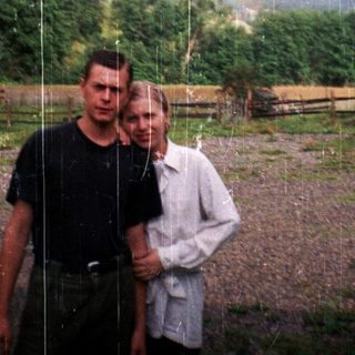 Two people standing in rain, rural countryside background.