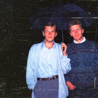Two men standing together under an umbrella.