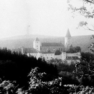 Historic castle complex in wooded hilly landscape.