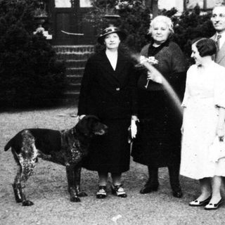 Family portrait with dog in early 20th-century garden setting.