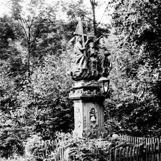 Historical monument with religious sculpture in wooded area.