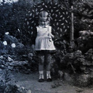 Young girl standing outdoors near tree and rocks.