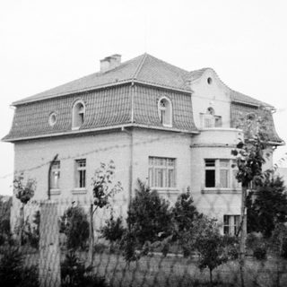 Two-story house with mansard roof, arched windows, aged exterior.