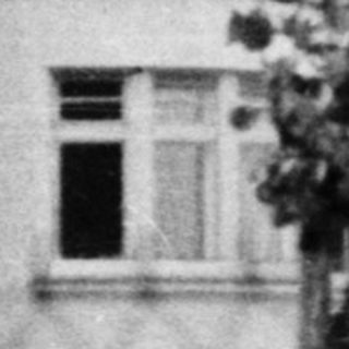 Two-story house with mansard roof, arched windows, aged exterior.