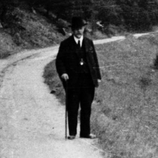 Two individuals walking along a rural dirt road near water.