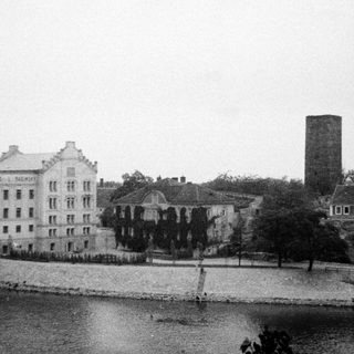 Historic building complex by waterfront with industrial chimney.