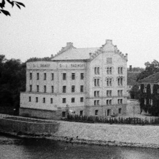 Historic building complex by waterfront with industrial chimney.