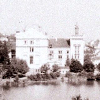 Building across a lake, with trees and people in foreground.