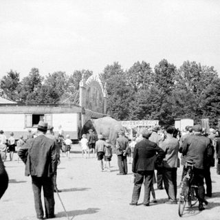 Group of men gather near a circus or fairground.