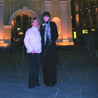 Two people stand in the rain near a building.