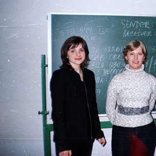 Three women stand in front of a blackboard with writing.
