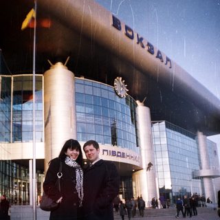 Couple poses in front of a large, modern train station.