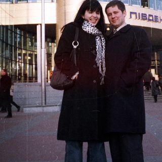 Couple poses in front of a large, modern train station.