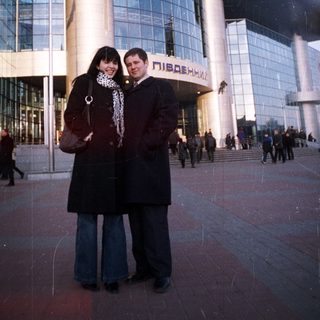 Couple poses in front of a large, modern train station.