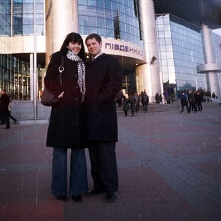 Couple poses in front of a large, modern train station.