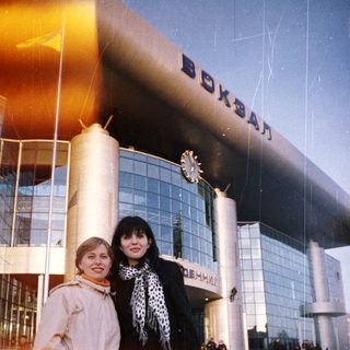 Two women stand in front of a large train station.