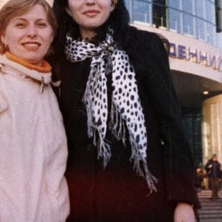 Two women stand in front of a large train station.