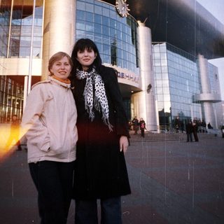 Two women stand in front of a large train station.