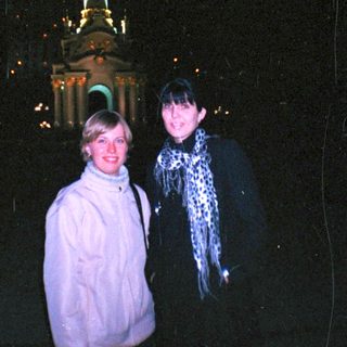 Here's a brief summary of the image: Two women stand near a lit monument at night.