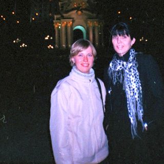 Here's a brief summary of the image: Two women stand near a lit monument at night.
