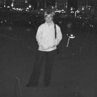 Man stands in front of brightly lit city buildings at night.