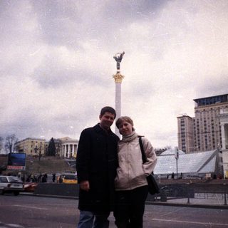 Couple stands near a monument in a city square.