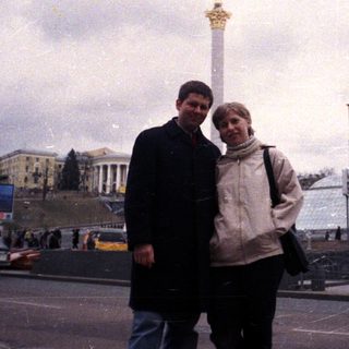 Couple stands near a monument in a city square.