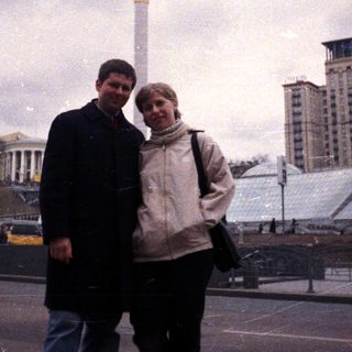 Couple stands near a monument in a city square.