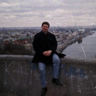 Man sits on a ledge overlooking a city and water.