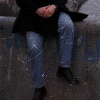 Man sits on a ledge overlooking a city and water.