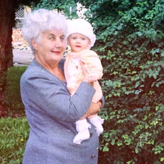 Woman in coat holds baby outdoors in a garden.