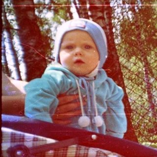 Two babies in a stroller outdoors, surrounded by trees.