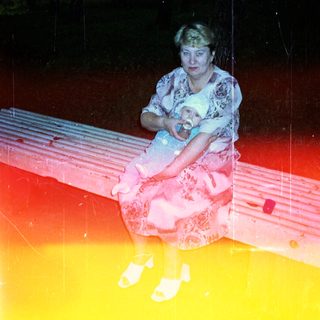Woman sits on a bench holding a baby in a forest.