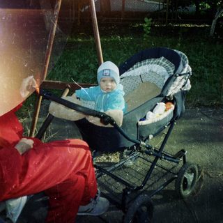 Baby in a stroller sits outside on a sunny day.