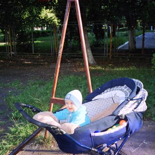 Baby in a stroller sits outdoors near a fence.